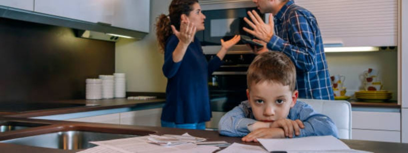 unhappy couple arguing in their kitchen with their young son seated at the table in front of them